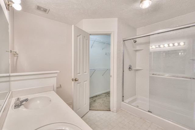 full bathroom featuring a textured ceiling, a sink, visible vents, a stall shower, and a walk in closet