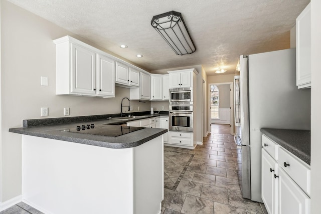 kitchen featuring dark countertops, a peninsula, black electric cooktop, white cabinetry, and a sink