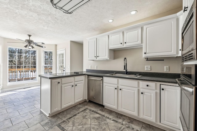 kitchen featuring dark countertops, a peninsula, appliances with stainless steel finishes, and a sink