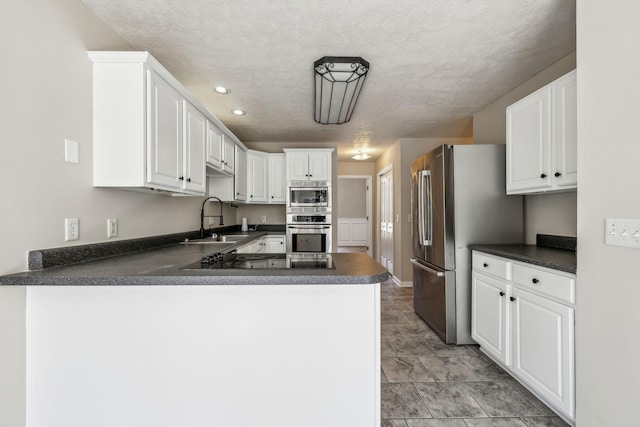 kitchen featuring white cabinets, dark countertops, appliances with stainless steel finishes, a peninsula, and a sink