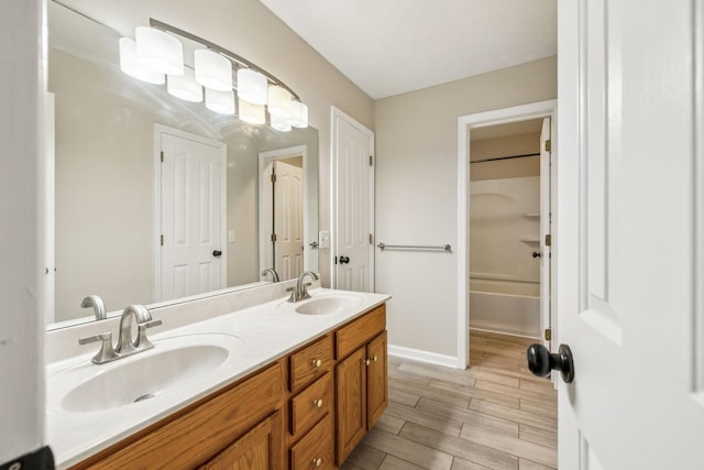 full bath featuring double vanity, wood finish floors, a sink, and baseboards