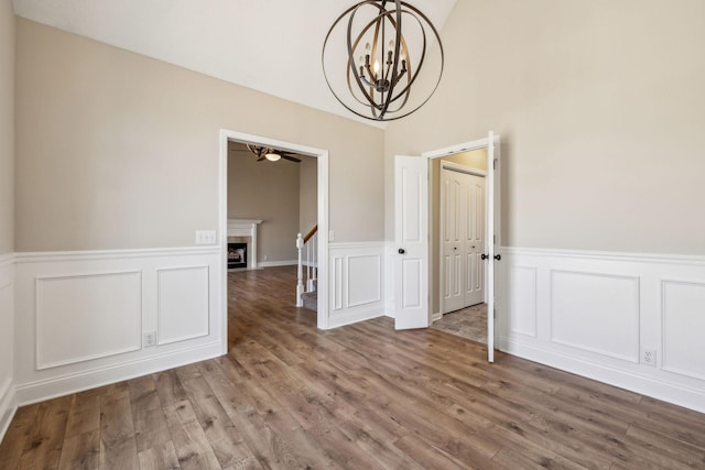 unfurnished dining area with stairs, a fireplace, wood finished floors, and an inviting chandelier