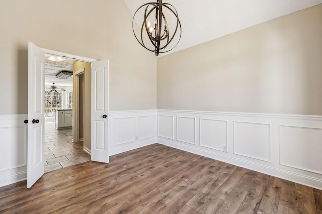 empty room with wainscoting, wood finished floors, and a notable chandelier