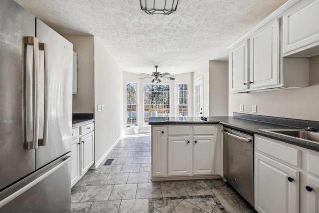 kitchen featuring a peninsula, appliances with stainless steel finishes, dark countertops, and white cabinets