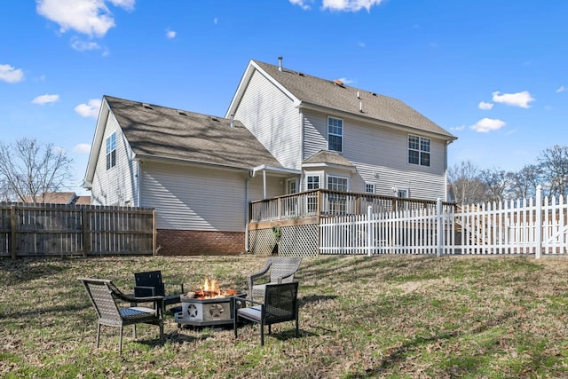 rear view of property featuring a fire pit, a yard, a shingled roof, and fence