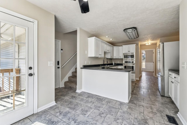 kitchen with a peninsula, a sink, white cabinetry, appliances with stainless steel finishes, and dark countertops