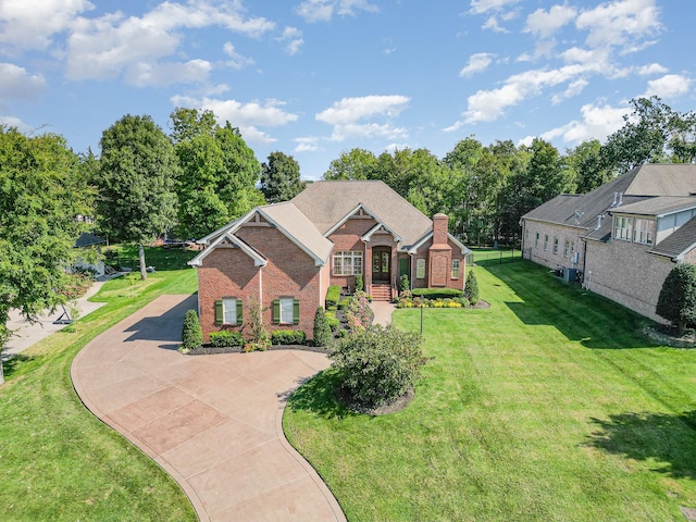 view of front of home with driveway, brick siding, a chimney, and a front yard