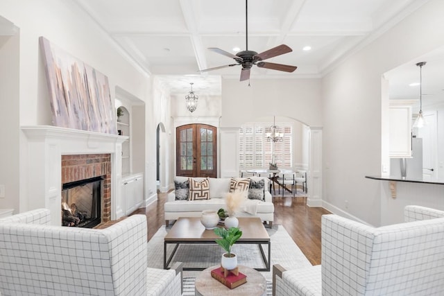 living room featuring arched walkways, beam ceiling, a fireplace, wood finished floors, and coffered ceiling