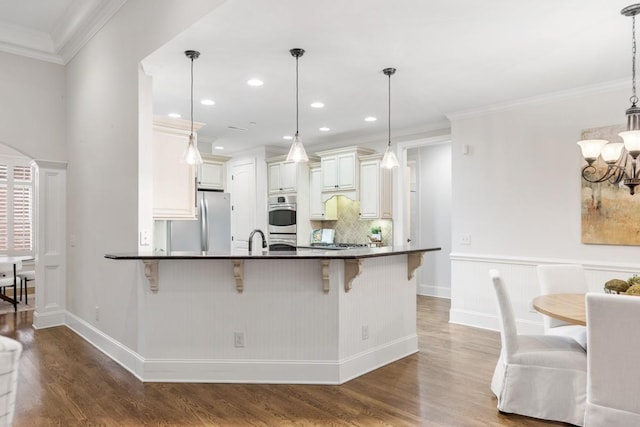 kitchen with a breakfast bar, wood finished floors, ornamental molding, appliances with stainless steel finishes, and dark countertops