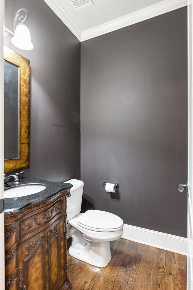 bathroom featuring baseboards, toilet, ornamental molding, wood finished floors, and vanity