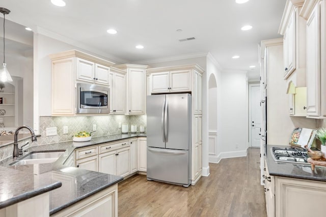 kitchen featuring arched walkways, ornamental molding, stainless steel appliances, light wood-type flooring, and a sink