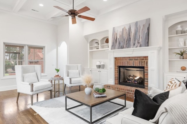 interior space with coffered ceiling, wood finished floors, built in features, a brick fireplace, and beamed ceiling