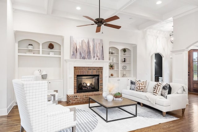 living area with arched walkways, built in shelves, coffered ceiling, wood finished floors, and beam ceiling