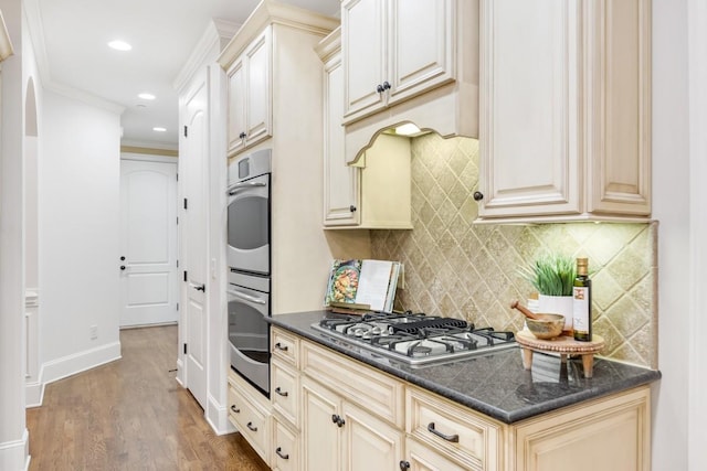 kitchen with stainless steel appliances, cream cabinetry, dark countertops, and wood finished floors