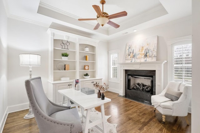 office area featuring a tray ceiling, crown molding, a fireplace, wood finished floors, and baseboards