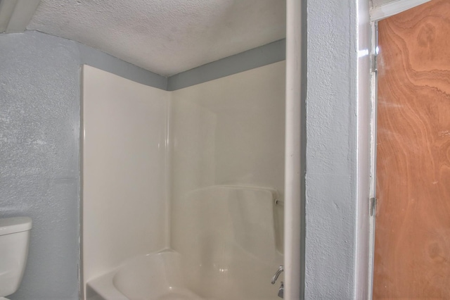 bathroom featuring  shower combination, a textured wall, a textured ceiling, and toilet