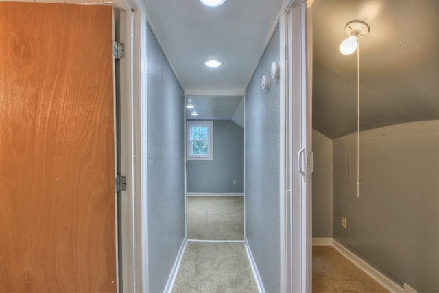 corridor featuring lofted ceiling, carpet, baseboards, and a textured wall