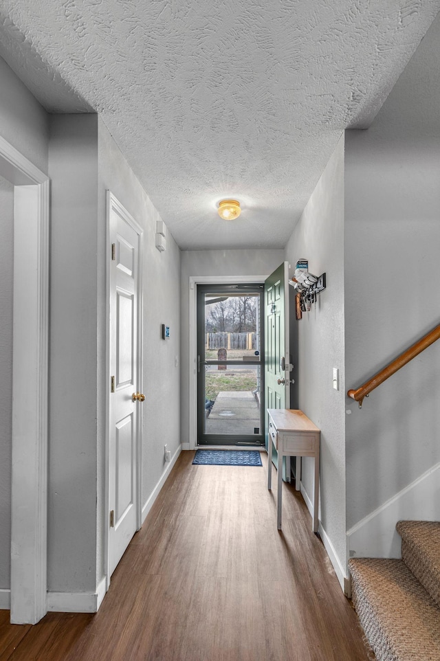 entryway with a textured ceiling, stairs, baseboards, and wood finished floors