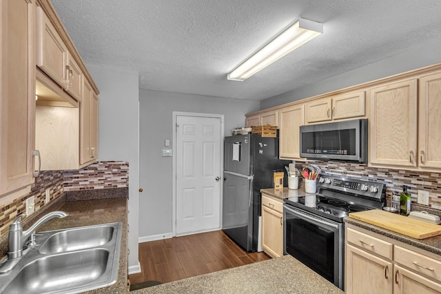 kitchen featuring light brown cabinets, stainless steel appliances, a sink, backsplash, and dark wood-style floors