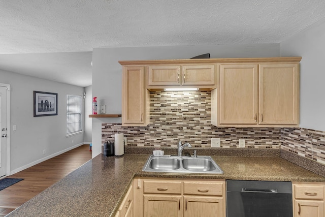 kitchen with light brown cabinetry, dark countertops, a sink, and dishwashing machine