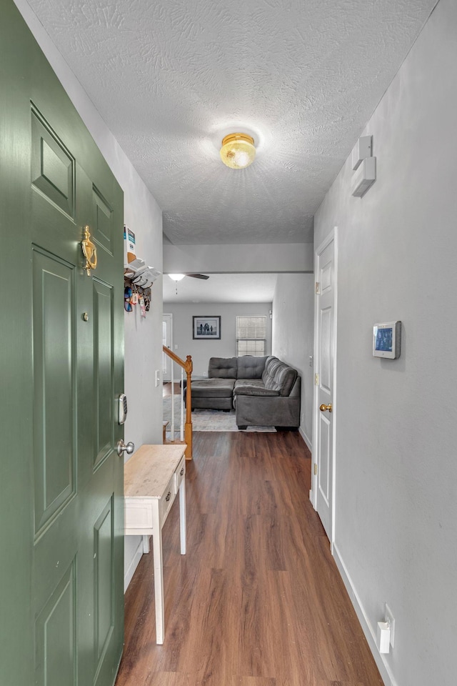 corridor featuring stairs, baseboards, dark wood finished floors, and a textured ceiling