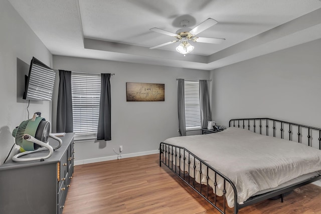 bedroom featuring a raised ceiling, baseboards, ceiling fan, and light wood finished floors