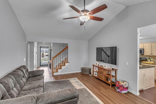 living area with ceiling fan, vaulted ceiling, wood finished floors, baseboards, and stairs