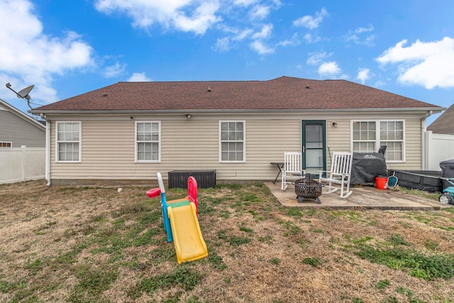 back of house featuring a patio, a fire pit, a shingled roof, fence, and a yard