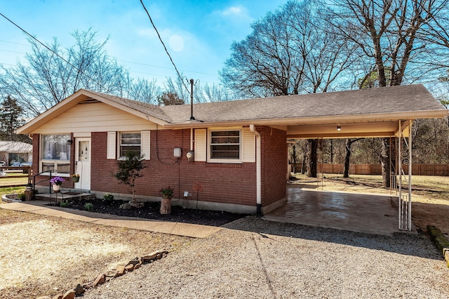 view of front facade with driveway, an attached carport, roof with shingles, fence, and brick siding