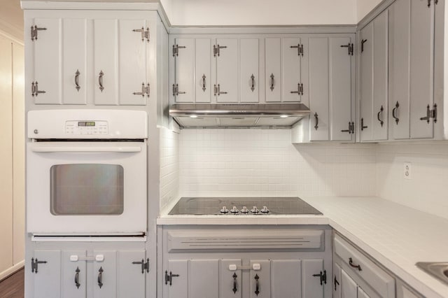 kitchen with black electric stovetop, light countertops, decorative backsplash, oven, and under cabinet range hood