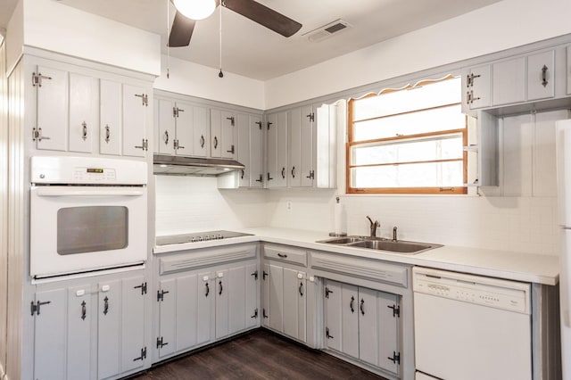 kitchen with under cabinet range hood, white appliances, dark wood-type flooring, a sink, and visible vents