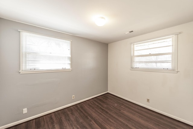 unfurnished room with baseboards, visible vents, and dark wood finished floors