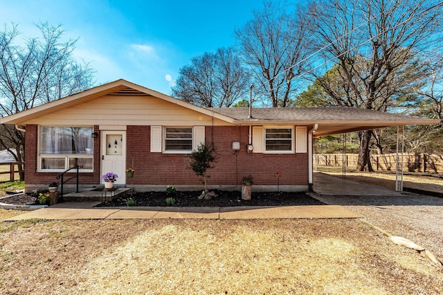 view of front of house featuring an attached carport, brick siding, driveway, and fence