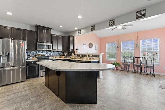 kitchen featuring a kitchen island, appliances with stainless steel finishes, a sink, light countertops, and backsplash