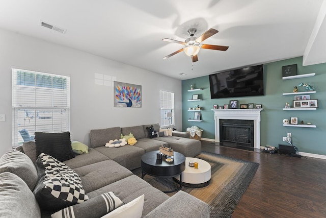 living area featuring ceiling fan, a fireplace, wood finished floors, visible vents, and baseboards