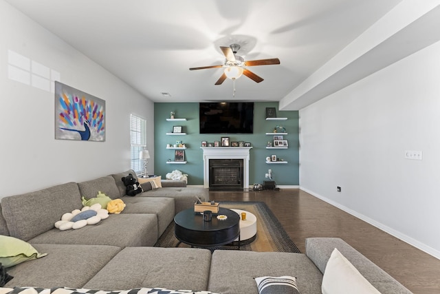 living room featuring ceiling fan, a fireplace, baseboards, and wood finished floors