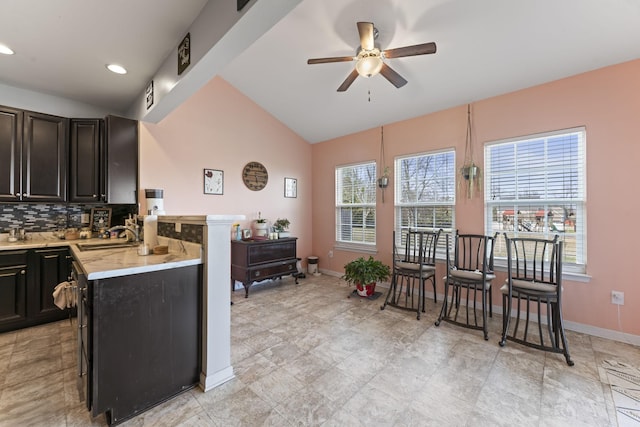 kitchen with baseboards, ceiling fan, a sink, vaulted ceiling, and backsplash