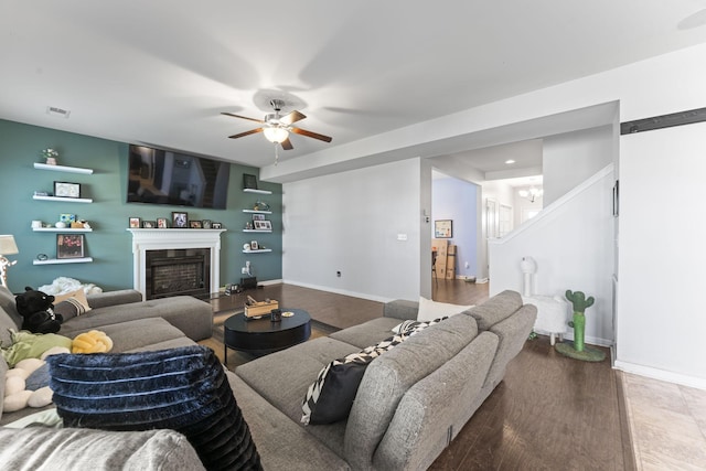 living room featuring ceiling fan, a fireplace, baseboards, and wood finished floors