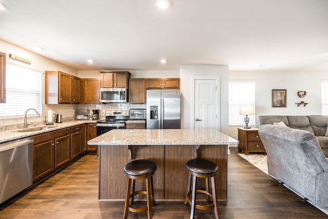 kitchen featuring stainless steel appliances, a sink, a kitchen island, open floor plan, and dark wood-style floors