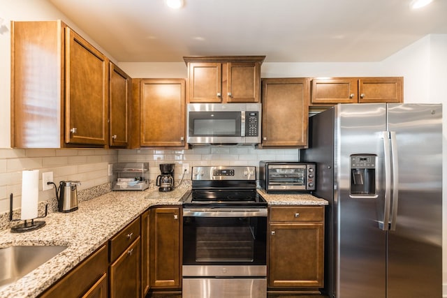 kitchen featuring a toaster, decorative backsplash, appliances with stainless steel finishes, light stone countertops, and a sink