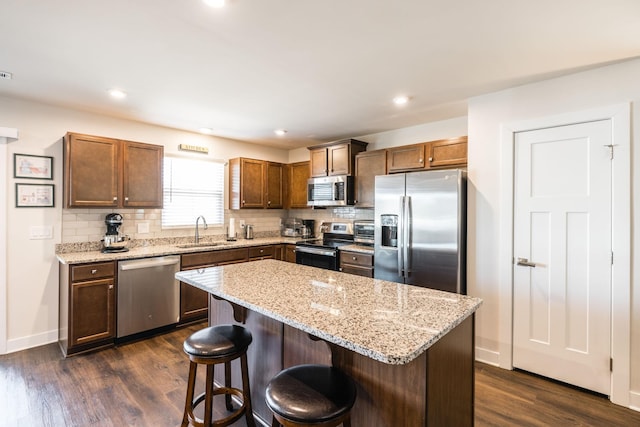 kitchen with dark wood-type flooring, a sink, a kitchen breakfast bar, appliances with stainless steel finishes, and decorative backsplash