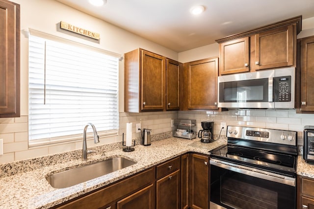 kitchen with appliances with stainless steel finishes, a sink, backsplash, and light stone countertops