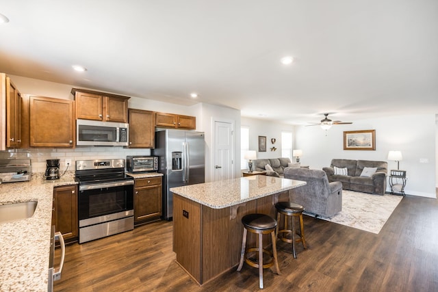 kitchen with a kitchen bar, stainless steel appliances, dark wood finished floors, and a center island