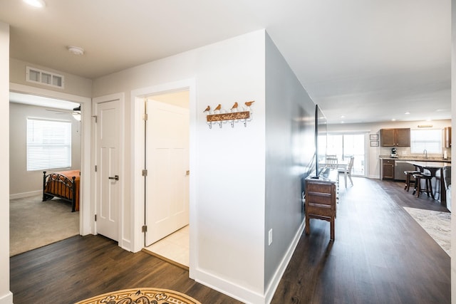 hallway featuring a sink, baseboards, visible vents, and dark wood-style flooring