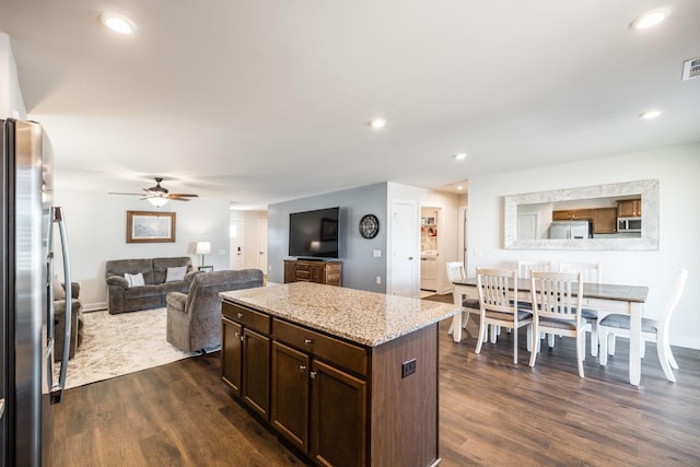 kitchen with dark wood-style floors, a center island, appliances with stainless steel finishes, open floor plan, and light stone countertops