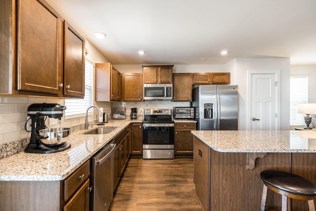 kitchen featuring dark wood-style floors, appliances with stainless steel finishes, light stone counters, a kitchen bar, and a sink