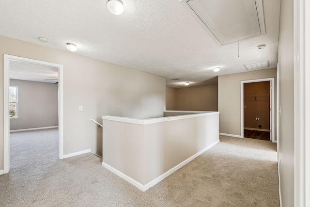 hall featuring a textured ceiling, an upstairs landing, baseboards, carpet, and attic access