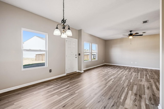 empty room featuring baseboards, visible vents, wood finished floors, and ceiling fan with notable chandelier