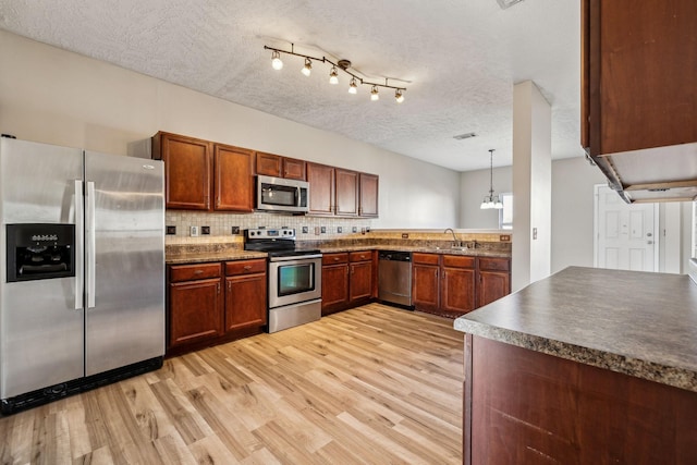 kitchen with decorative backsplash, dark countertops, light wood-style flooring, appliances with stainless steel finishes, and a sink