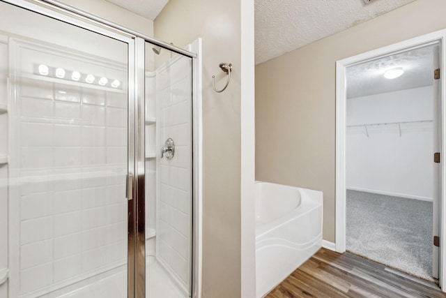 bathroom with wood finished floors, a garden tub, a walk in closet, a textured ceiling, and a shower stall